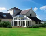 Une **veranda angle maison** moderne, avec une structure vitrée lumineuse, s'intègre parfaitement à l'architecture de la demeure.
