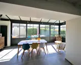 Salle à manger lumineuse dans une véranda chauffée, avec une table en bois et des chaises colorées. Un espace de vie agréable.