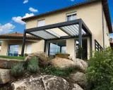 Pergola moderne sur terrasse avec vue sur une maison et un jardin rocheux.