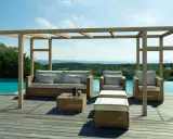 Salon extérieur avec mobilier en rotin sous une pergola en bois. La hauteur de la pergola en bois offre une ombre agréable sur la terrasse en bois, près de la piscine.