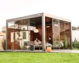 Un couple se détend dans une pergola moderne avec parois vitrées. La fixation pergola est discrète, laissant place à un espace cosy avec chauffage d'appoint.