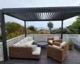 Un salon d'extérieur confortable sous une pergola sur toit terrasse, avec vue sur la mer.