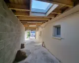 Couloir en construction, partie d'une extension maison, avec murs en parpaings, plafond en bois, fenêtre de toit et matériaux de chantier.