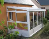 Une véranda démontable sans permis de construire, avec chaises longues et table à manger, prolonge la maison pour profiter du jardin.