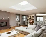 Un salon moderne avec un grand puit de lumière au plafond, un canapé confortable, une cheminée et une cuisine ouverte.
