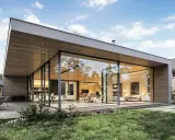 Une extension maison contemporaine avec de grandes baies vitrées, une terrasse en bois et un jardin verdoyant. L'intérieur lumineux révèle un salon et une cuisine modernes.