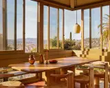 Une salle à manger lumineuse dans une veranda sur terrasse en bois, avec vue panoramique sur la ville et les palmiers.