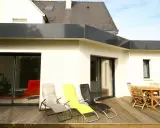 Extension de toit plat en bac acier, avec terrasse en bois, chaises longues et table de jardin.