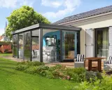 Une élégante veranda independante de la maison, avec une salle à manger et un salon d'extérieur, entourée d'un jardin verdoyant.