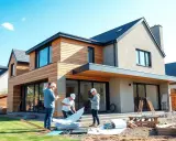 Trois hommes discutent des plans d'une extension de maison de 20m2 devant une maison moderne en bois et pierre.