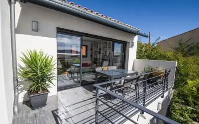 Terrasse sur le toit accessible, avec table et chaises, et une grande baie vitrée donnant sur un salon rempli de livres.