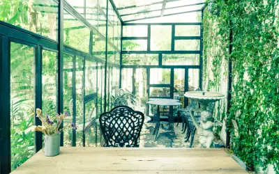 Un charmant jardin d'hiver verrière, avec des tables et chaises en fer forgé, une statue d'ange et une profusion de verdure.