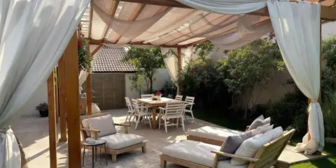 Une belle idée pergola jardin avec salon de jardin, chaises et table à manger, le tout sous des voilages légers.