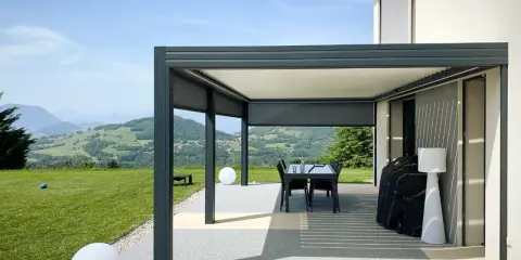 Pergola bioclimatique moderne face à un paysage vallonné. Le vent fort fait onduler les lames du toit, créant des jeux d'ombre et de lumière.