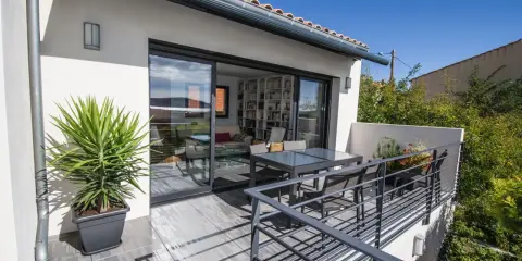 Terrasse sur le toit accessible, avec table et chaises, et une grande baie vitrée donnant sur un salon rempli de livres.