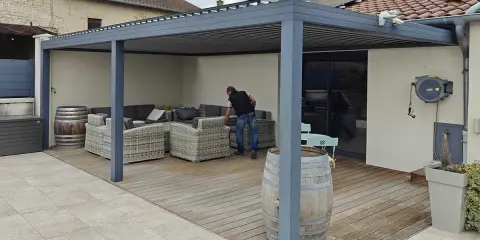 Installation d'un auvent sans permis de construire. Un homme arrange des coussins sur un canapé extérieur sous la structure moderne.