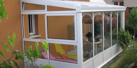 Une véranda démontable sans permis de construire, avec chaises longues et table à manger, prolonge la maison pour profiter du jardin.