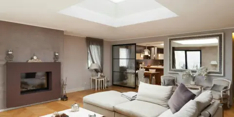 Un salon moderne avec un grand puit de lumière au plafond, un canapé confortable, une cheminée et une cuisine ouverte.