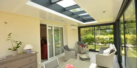 Une **veranda qui s'ouvre entièrement** sur un jardin verdoyant. Mobilier confortable, table et chaises pour profiter du soleil.
