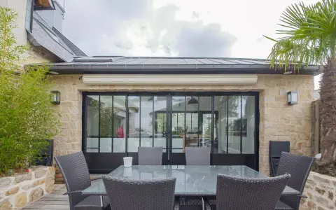 Terrasse avec mobilier autour d'une extension maison style atelier aux grandes verrières noires. Bambou et palmier apportent une touche végétale.