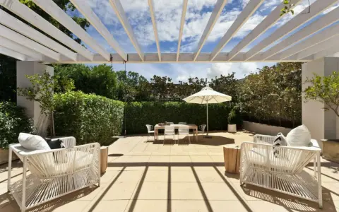 Terrasse couverte avec pergola blanche, mobilier de jardin blanc, table et parasol. Un espace extérieur aménagé, peut-être pour fermer une terrasse couverte sans autorisation.