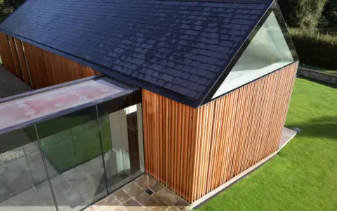 Vue aérienne d'un agrandissement maison sur le côté, avec bardage bois, toit en ardoises et extension vitrée.