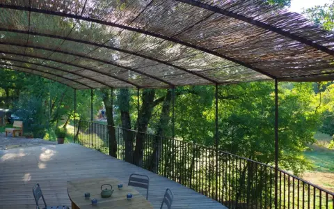 Vue d'une terrasse en bois sous une pergola recouverte de canisse. Le sens de pose de canisse sur pergola offre une ombre naturelle et agréable.