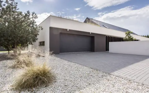 Moderne maison avec agrandissement garage, allée pavée, gravier blanc et végétation.