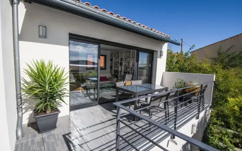 Terrasse sur le toit accessible, avec table et chaises, et une grande baie vitrée donnant sur un salon rempli de livres.