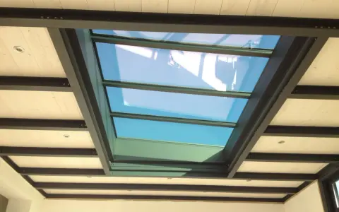 Veranda avec un grand puit de lumière vitré, illuminant un plafond en bois et poutres métalliques.