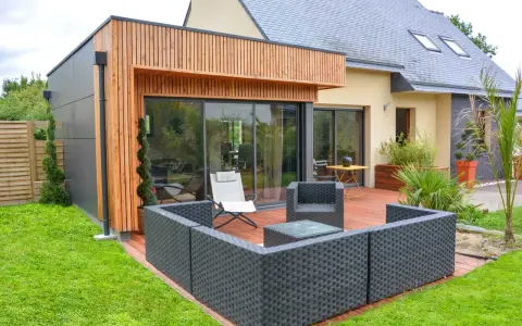 Une extension bois 30m2 moderne avec terrasse en bois, mobilier de jardin et grandes baies vitrées.