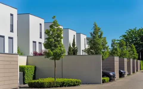 Lignes architecturales modernes, une extension accolée sur mur non mitoyen, des arbres et des voitures garées dans des box.