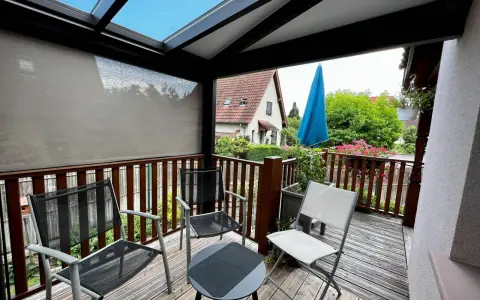 Un petit veranda balcon avec des chaises et une table, offrant une vue sur un jardin verdoyant et une maison.