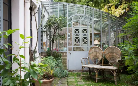 Une charmante veranda en fer forgé abrite un banc en rotin et des plantes luxuriantes, invitant à la détente dans ce jardin secret.