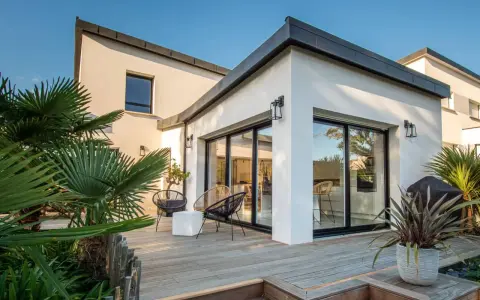 Une extension verrière moderne illumine cette maison ancienne, offrant une vue imprenable sur la terrasse en bois et le jardin luxuriant.