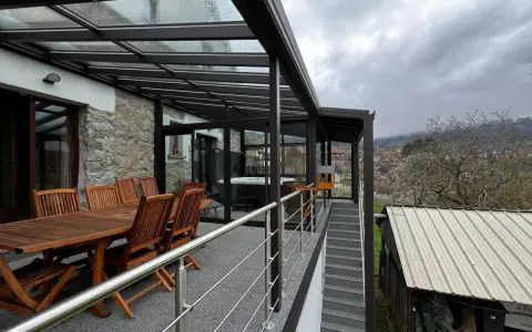 Veranda sur terrasse surélevée avec jacuzzi et table en bois. Vue sur un village et des collines brumeuses.