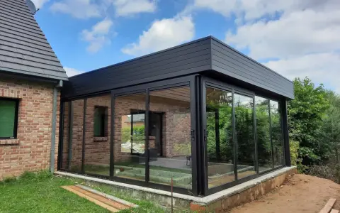Moderne véranda toit plat avec puits de lumière, offrant une vue panoramique sur le jardin. L'extension en verre et métal s'intègre parfaitement à la maison en briques.