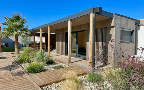 Maison moderne avec une extension toiture terrasse en bois, entourée d'un jardin paysager et d'une terrasse en bois.