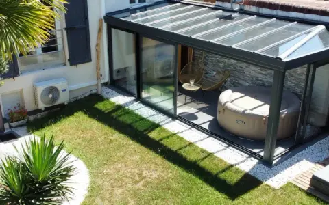 Une **veranda tuile** moderne avec jacuzzi et fauteuils, entourée d'un jardin verdoyant et d'une palme luxuriante.