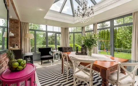 Une élégante verrière d'extension de maison baigne de lumière cette salle à manger, offrant une vue imprenable sur le jardin verdoyant.