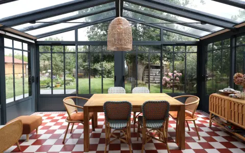Salle à manger lumineuse dans une véranda extension, avec table en bois, chaises colorées et vue sur le jardin.