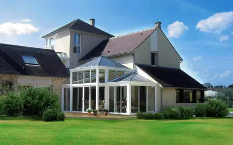 Une **veranda angle maison** moderne, avec une structure vitrée lumineuse, s'intègre parfaitement à l'architecture de la demeure.