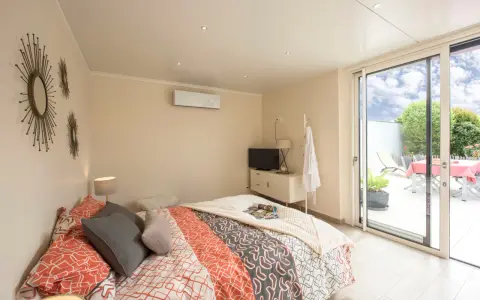 Chambre lumineuse d'une extension de maison, avec un lit confortable, une télévision et un accès direct à une terrasse extérieure.