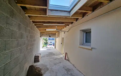 Vue d'une extension en cours de construction avec reprise de toiture, poutres apparentes et un puits de lumière.