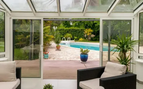 Une extension vitrée moderne s'ouvre sur une piscine et un jardin luxuriant, invitant à la détente.