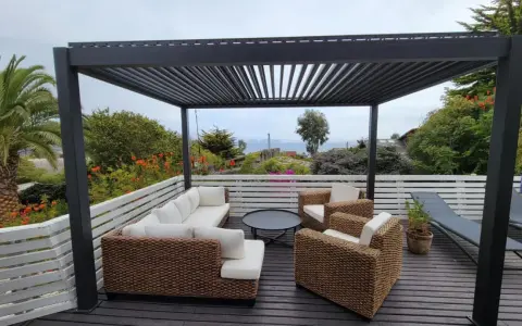 Un salon d'extérieur confortable sous une pergola sur toit terrasse, avec vue sur la mer.