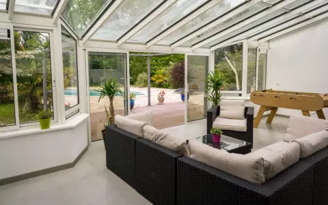 Vaste veranda 50m2 avec salon, baby-foot et vue sur piscine. Idéal pour se détendre et s'amuser en famille.