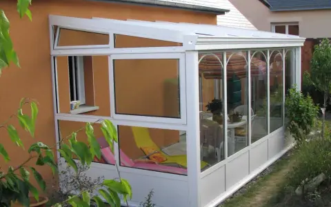 Une véranda démontable sans permis de construire, avec chaises longues et table à manger, prolonge la maison pour profiter du jardin.