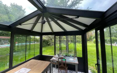 Intérieur d'une **veranda 2 pans** avec mobilier, sol décoratif et vue sur un jardin verdoyant.