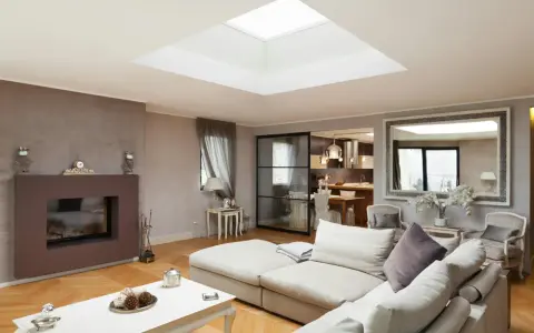 Un salon moderne avec un grand puit de lumière au plafond, un canapé confortable, une cheminée et une cuisine ouverte.